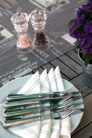 A table with a plate of folded napkins, a set of silverware, and a small potted plant with purple flowers. - Ringhotel Paulsen (Zeven)