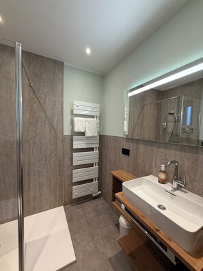 A modern bathroom with a glass shower enclosure, a white sink with a wooden vanity, and a towel rack with a white towel. - Ringhotel Paulsen (Zeven)