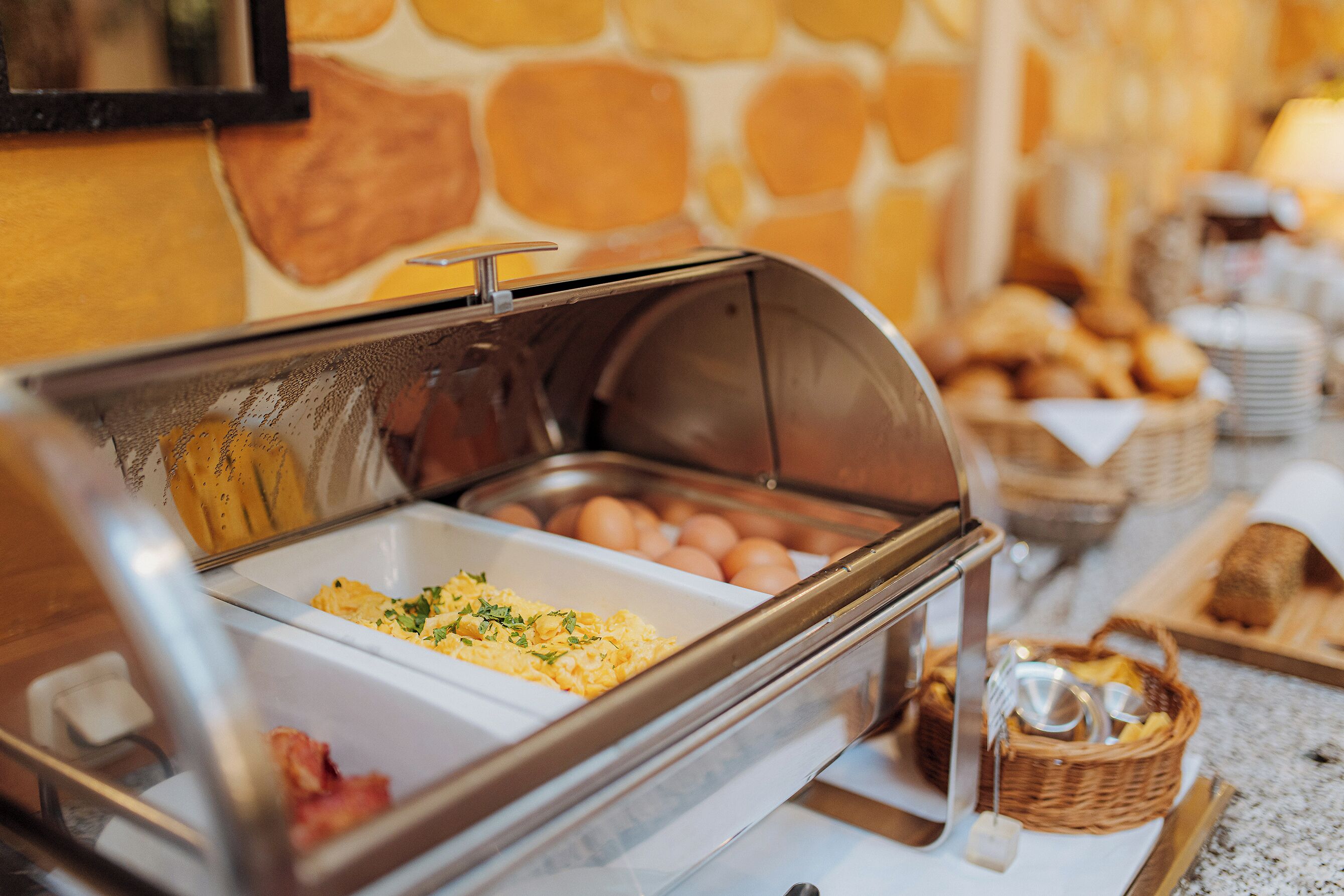 A buffet with scrambled eggs, eggs, and various breads.