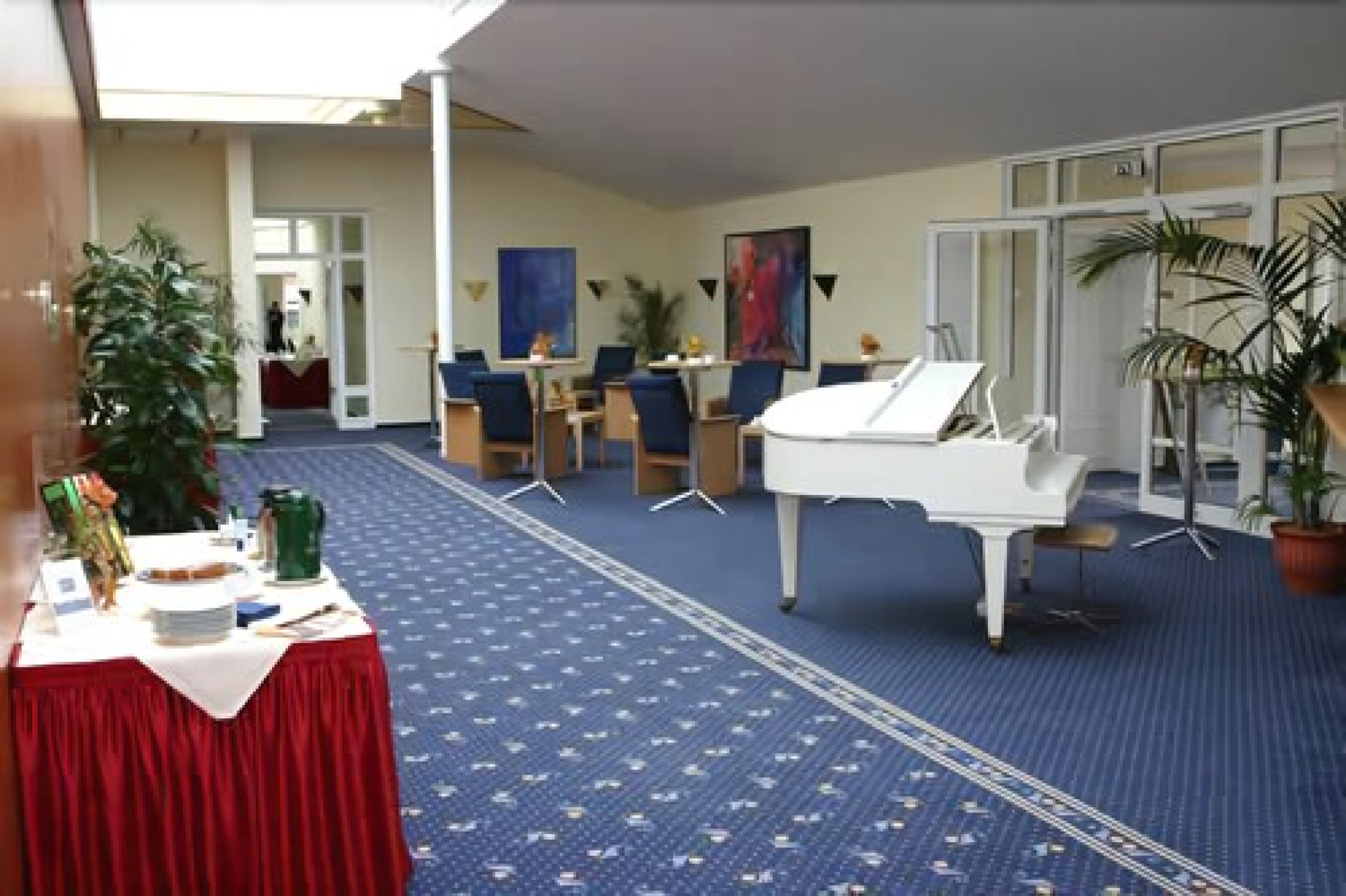 A room with a grand piano, a table with a red tablecloth, and several chairs.