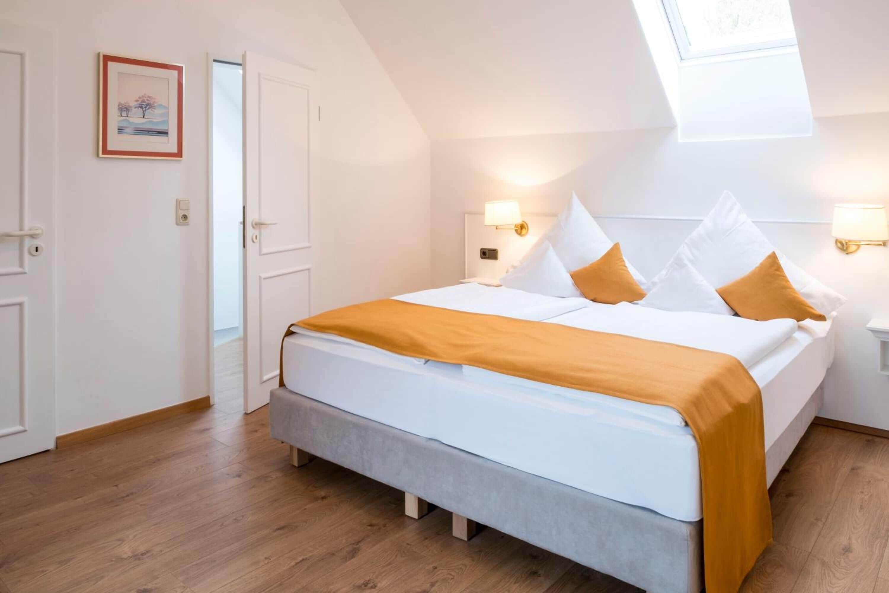 A bedroom with a bed, two bedside lamps, a window, and a door.
