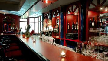 Uma área de bar com um bartender, um balcão comprido com copos e garrafas, e uma grande janela ao fundo.