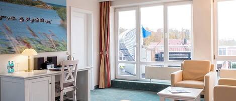 Habitación de hotel con cama, escritorio, silla, una mesita y un amplio ventanal con vistas a edificios y una bandera.