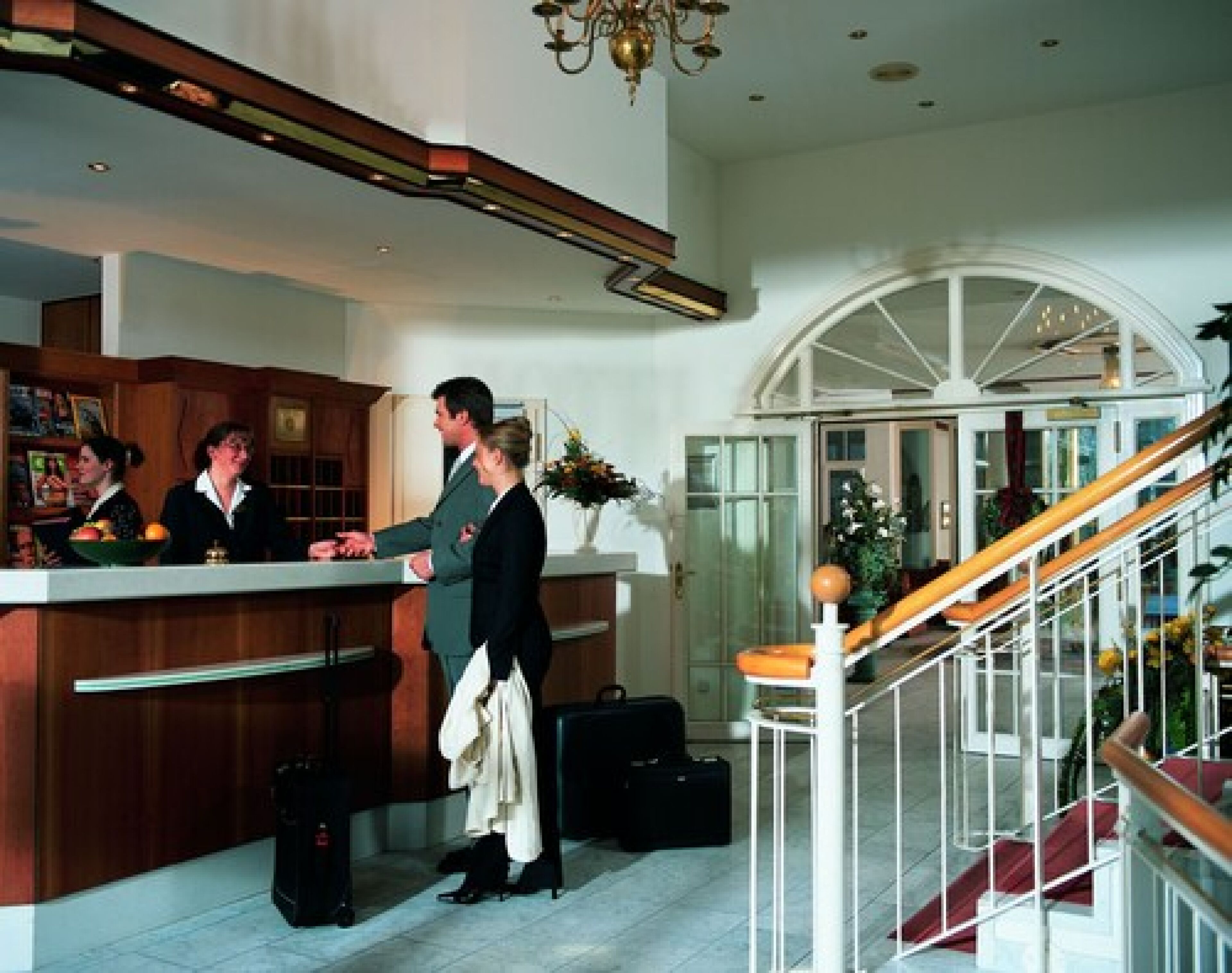 A hotel reception area with a counter, a staircase, and a large arched window.