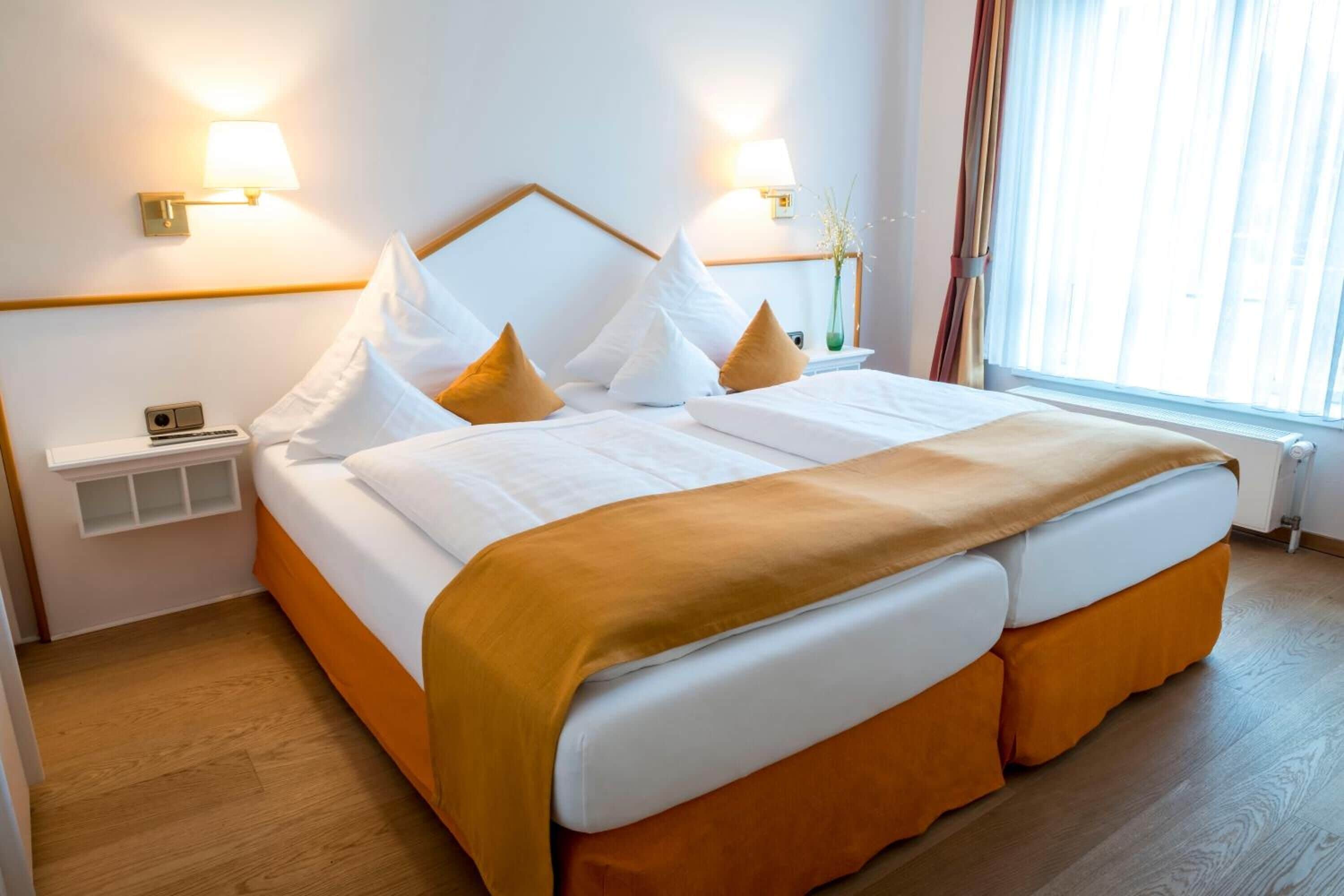 A hotel room with a large bed, two bedside lamps, a nightstand, and a window with curtains.