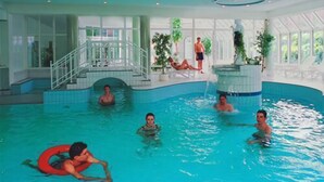 Una piscina interior con escalera central, varios niveles y un puesto de socorrista.