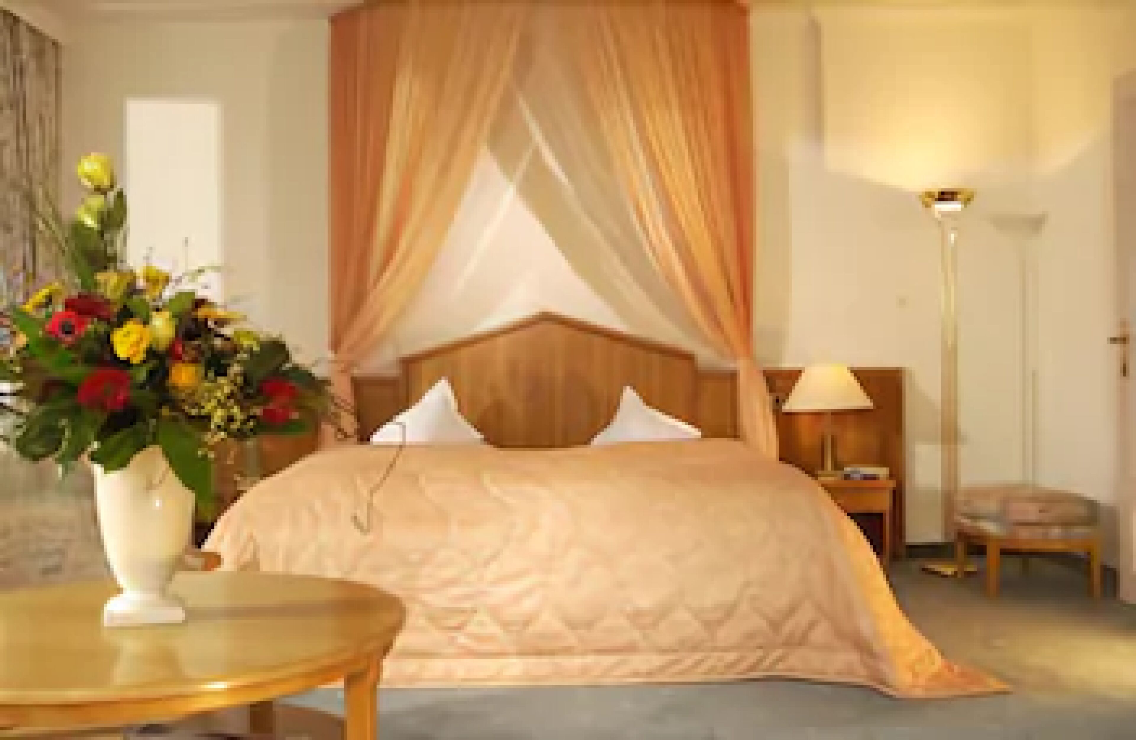 A bedroom with a bed, a bedside table, a lamp, and a vase with flowers.