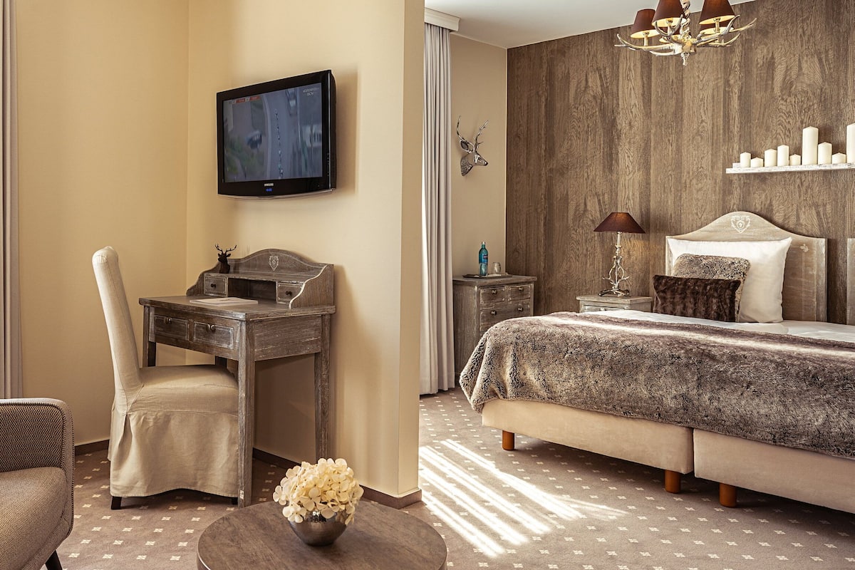 Une chambre d’hôtel comprenant un lit, un bureau, une chaise, une télévision, un lustre et une fenêtre avec des rideaux.