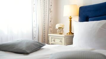 Ein ordentlich bezogenes Bett mit weißen und grauen Kissen, eine goldene Lampe auf einem weißen Nachttisch und ein blaues Kopfteil.