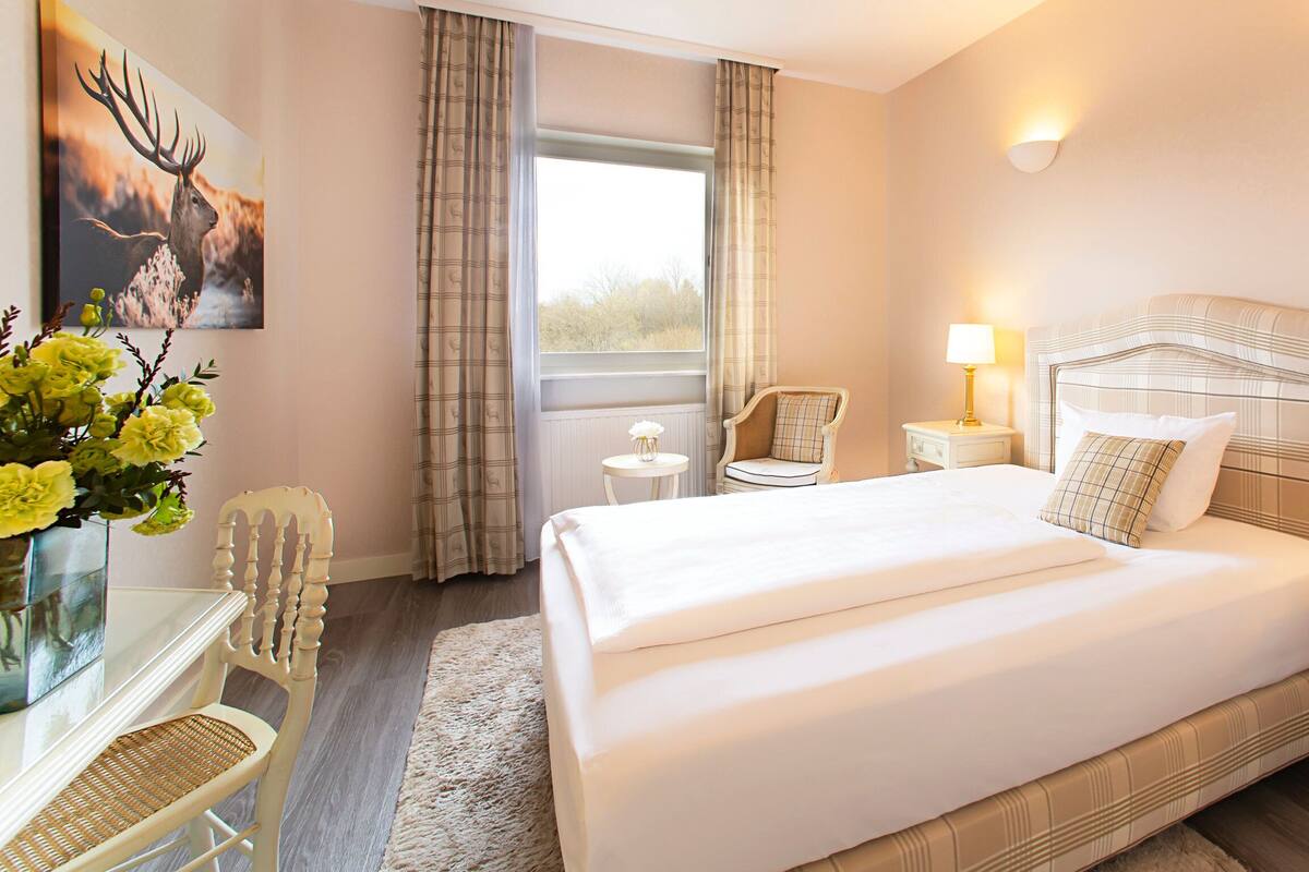 Une chambre d’hôtel avec un grand lit, deux tables de chevet, une chaise, une fenêtre avec des rideaux et une lampe fixée au mur.