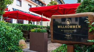 A welcome sign at a hotel entrance with outdoor seating and red umbrellas.