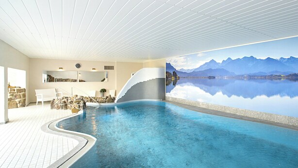 Una piscina interior con vistas a montañas y un lago.