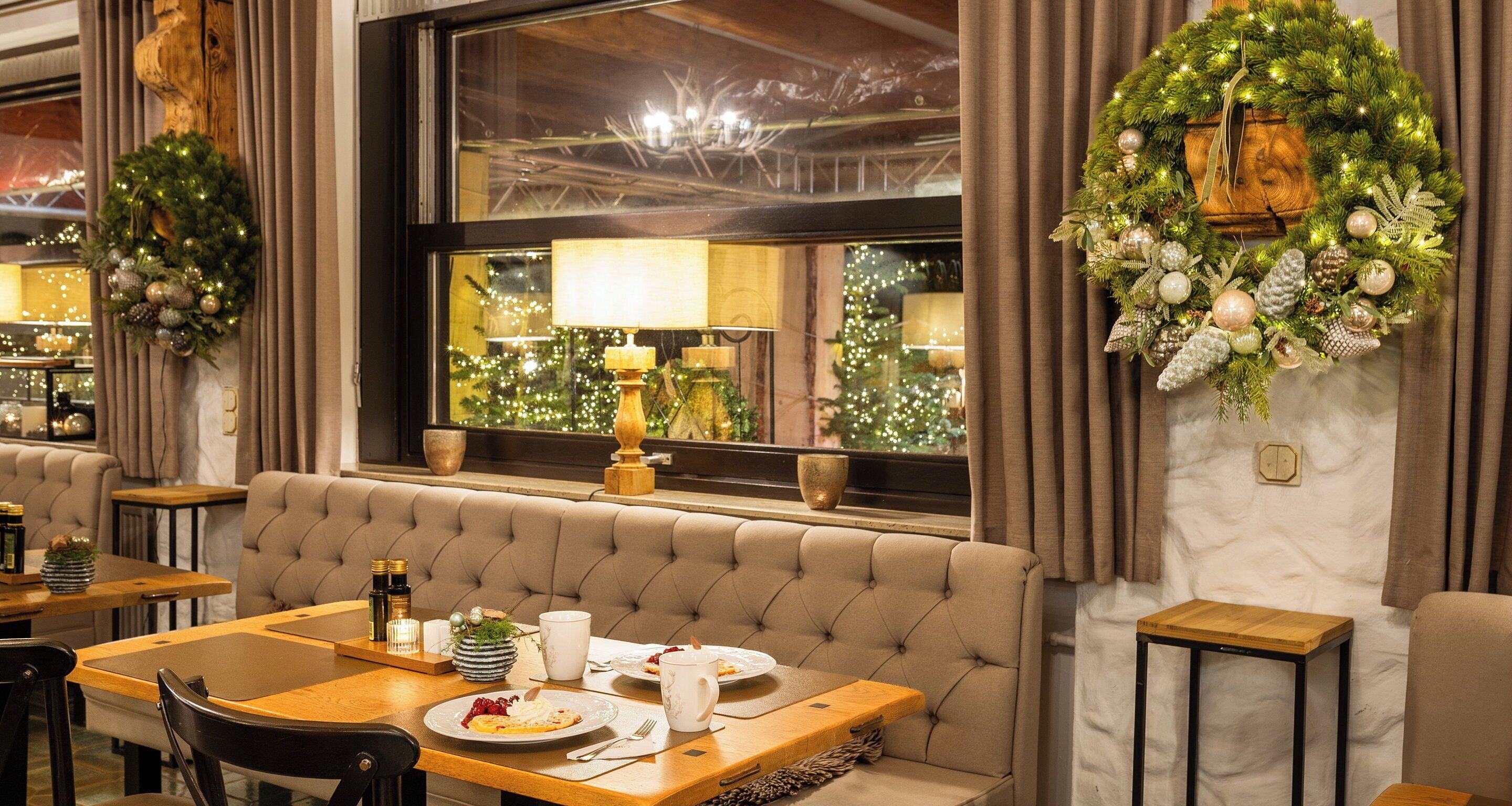 A dining area with a booth seating arrangement, a wooden table, and a view of a Christmas tree through a window.