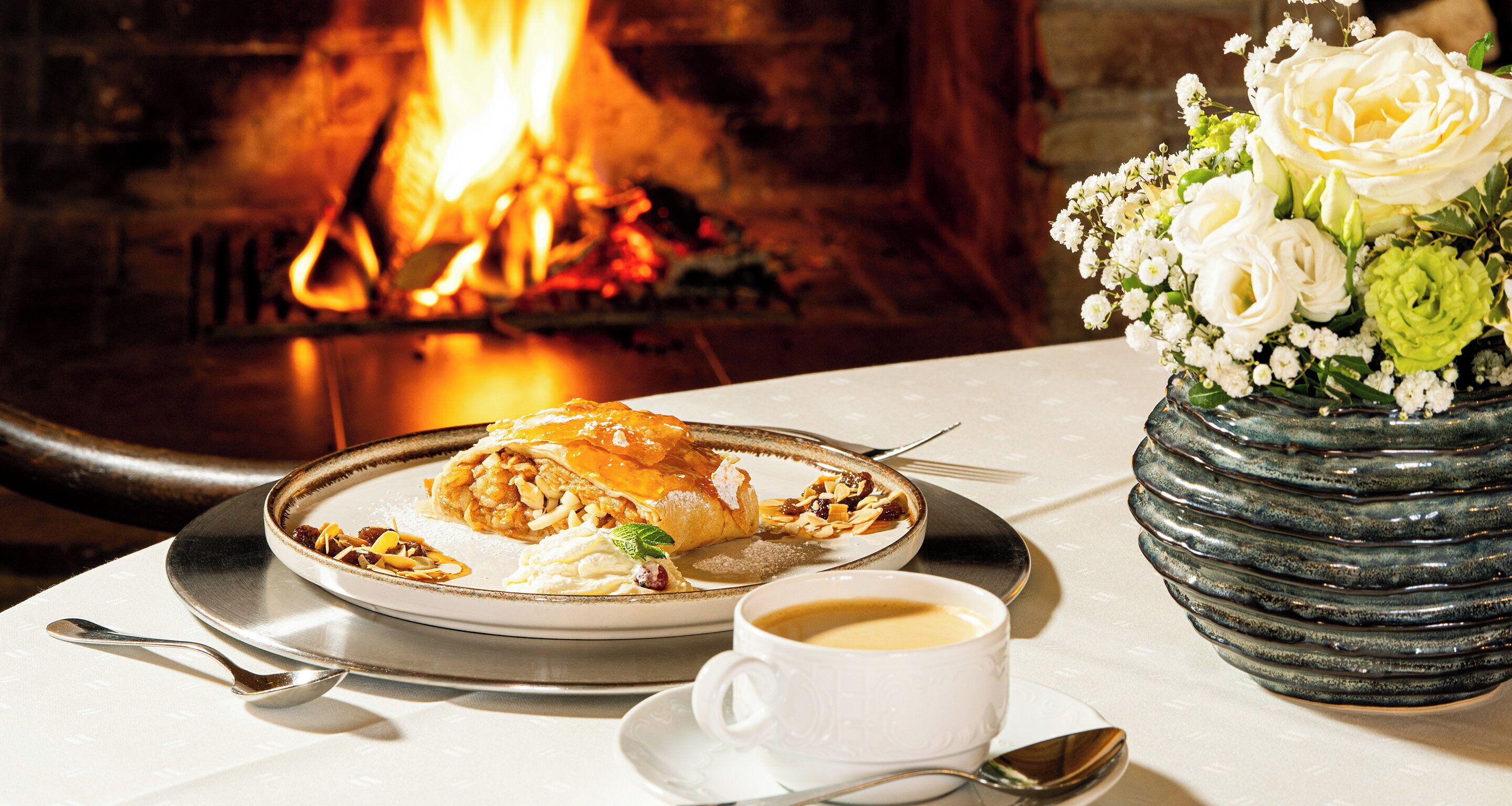 A dining table with a plate of food, a cup of coffee, and a vase of flowers.