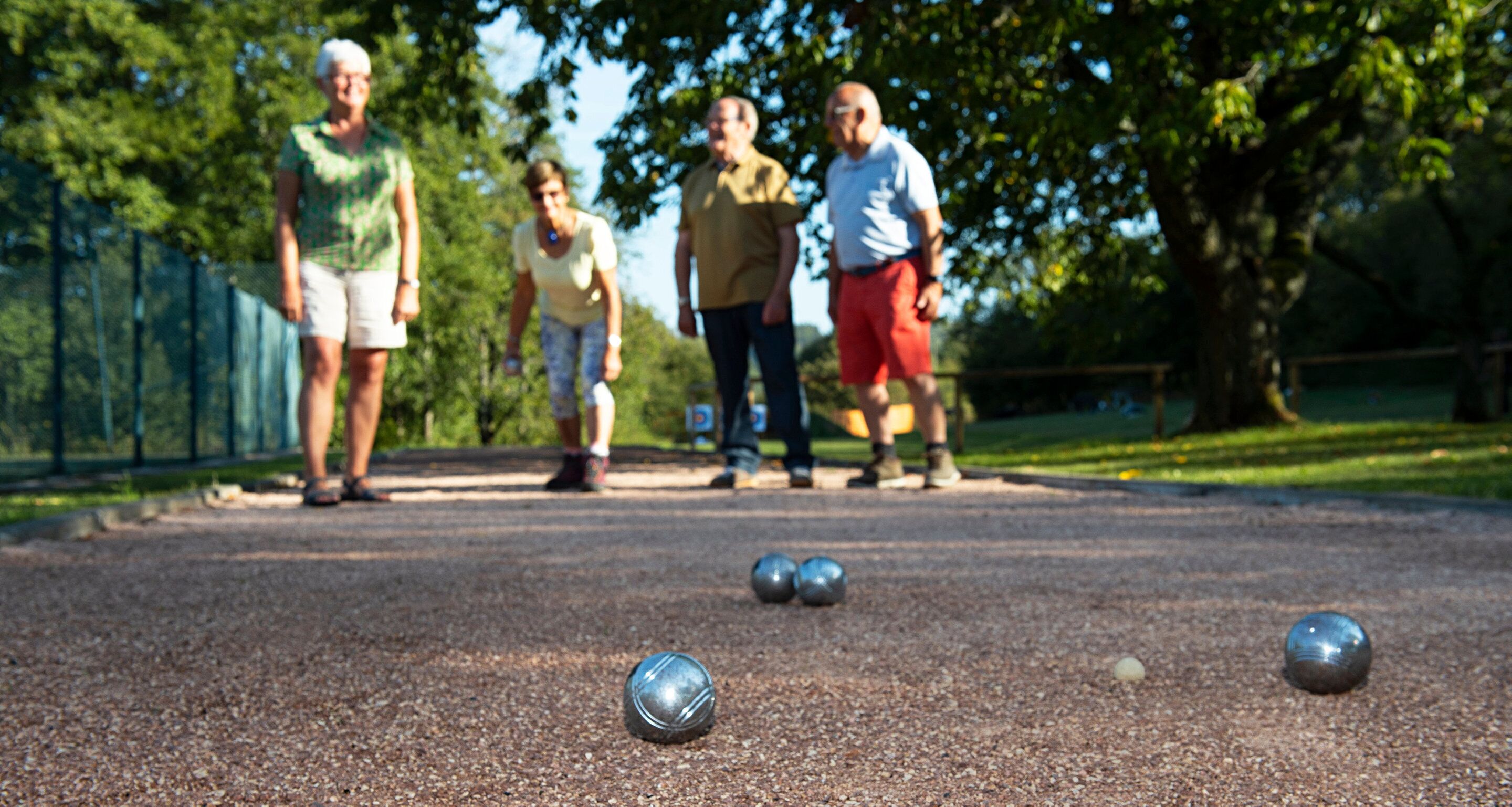 A group of people playing croquet on a gravel court with metal balls and a lawn ball.