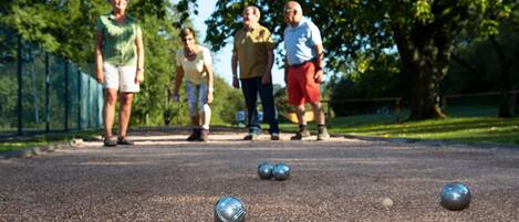 A group of people playing croquet on a gravel court with metal balls and a lawn ball.