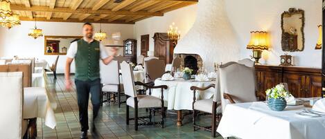 Interior de restaurante con vigas de madera, chimenea y mesas preparadas para comer.