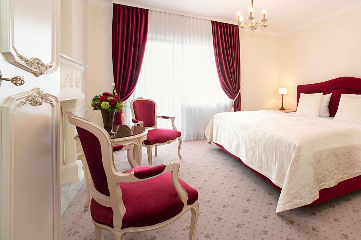 Une chambre d’hôtel dotée d’un grand lit, d’un coin salon avec un fauteuil et une table, ainsi que d’un miroir avec un cadre décoratif.