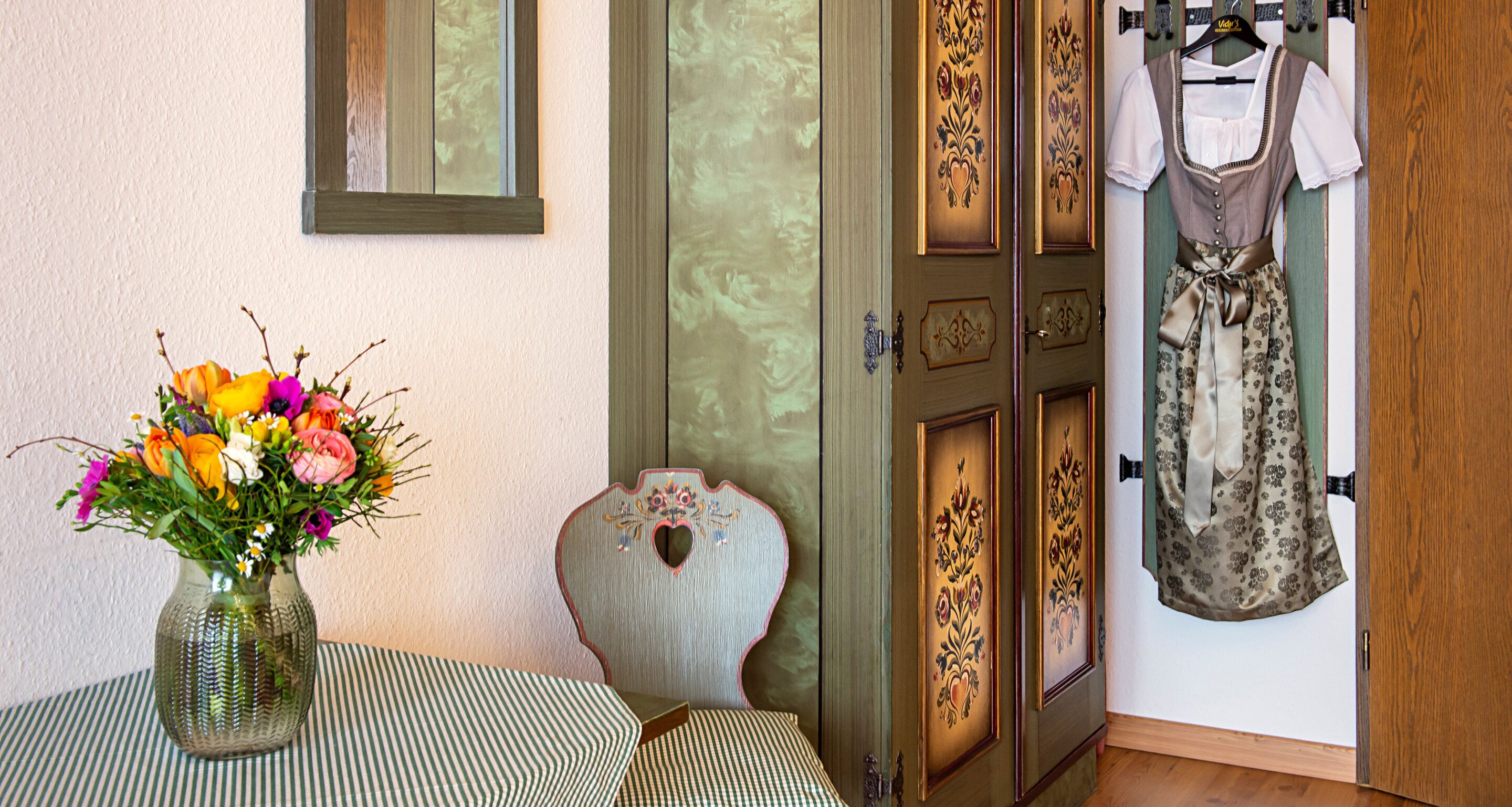 Una habitación con una puerta de madera, un jarrón de flores sobre una mesa y una prenda colgada.