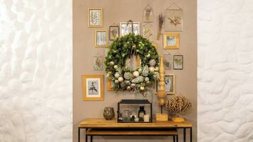 Una pared con impresiones botánicas enmarcadas, un adorno de piñas y una mesa de madera con una vela y un tarro de cristal.