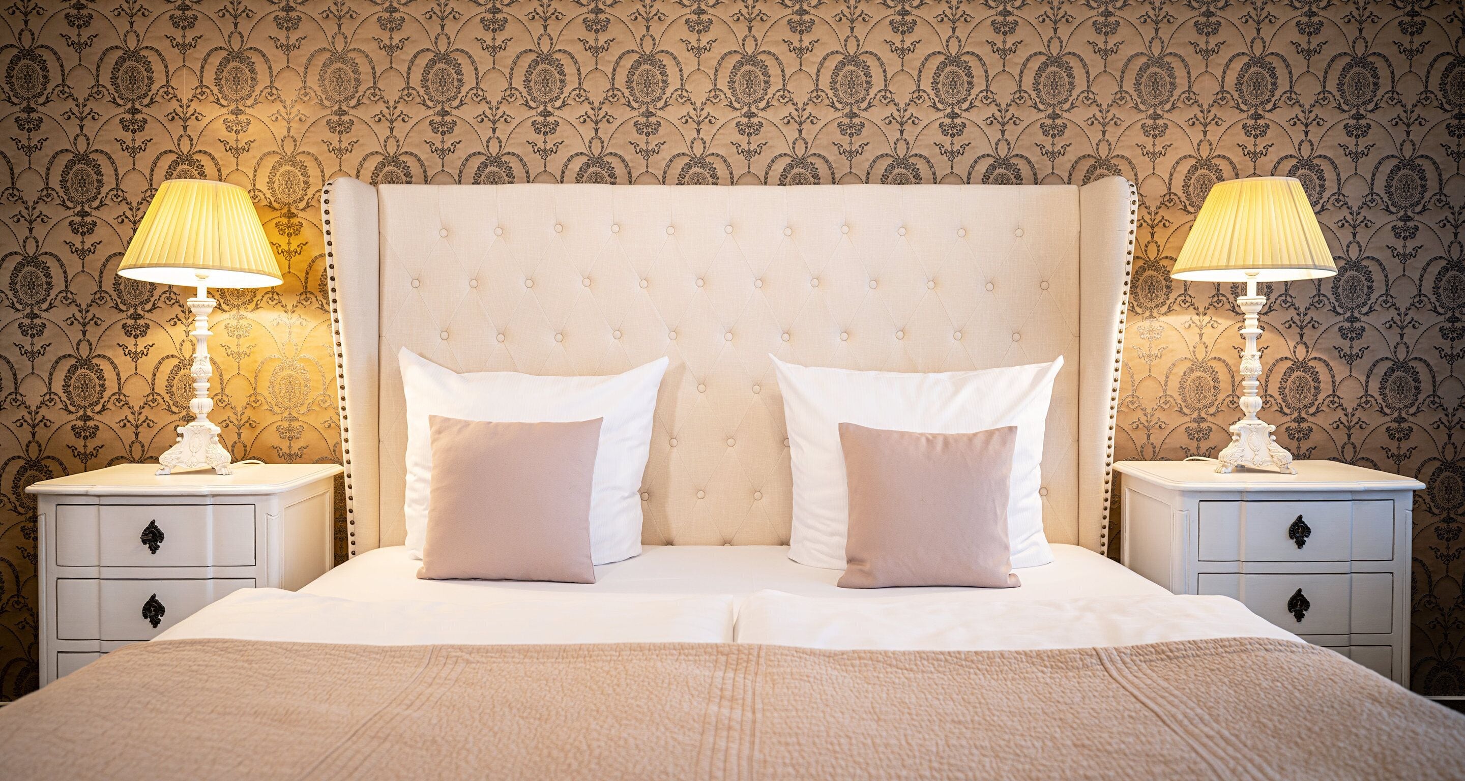 A neatly made bed with two pillows, a tufted headboard, and two bedside tables with lamps.