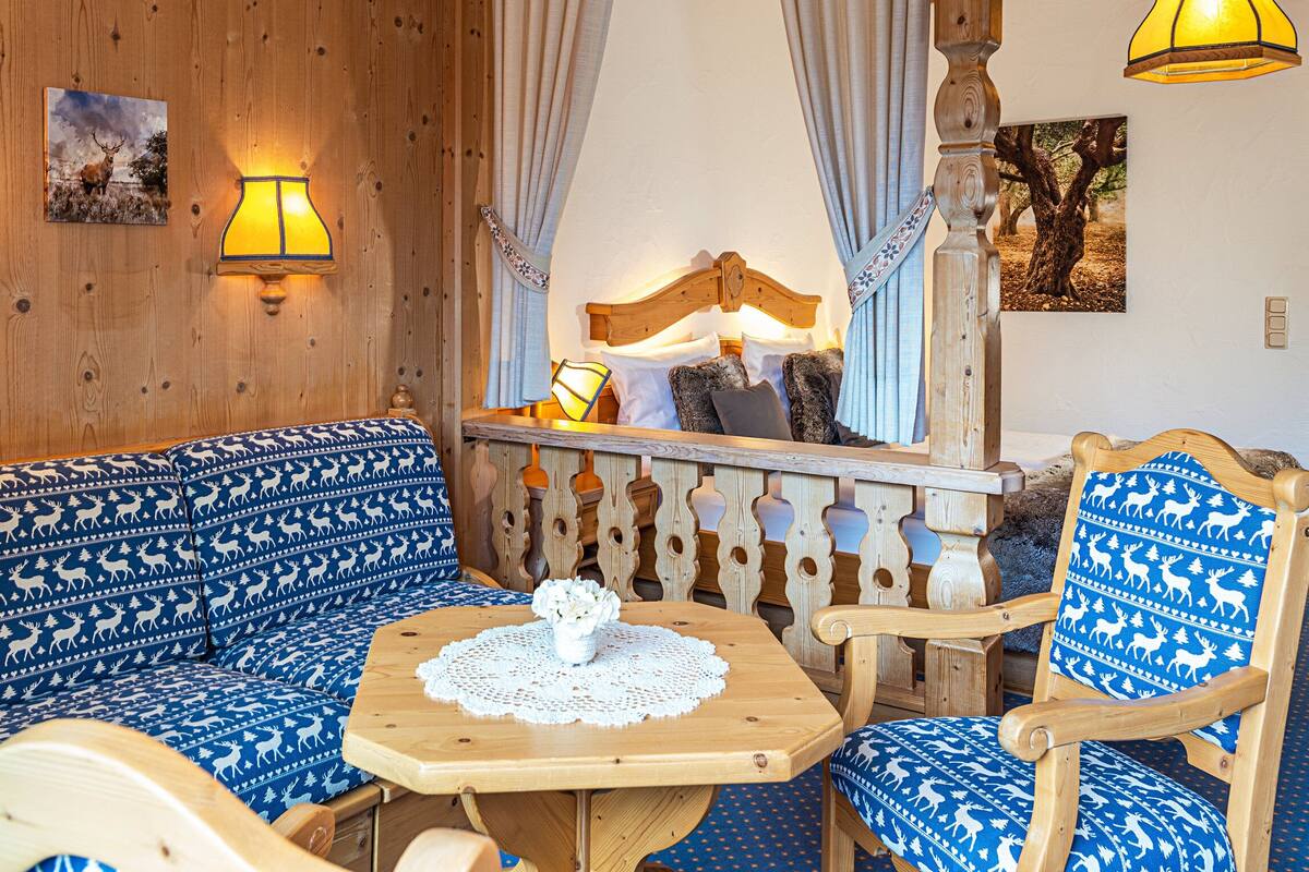 Une pièce chaleureuse avec un mur en bois, un canapé aux motifs bleus et blancs, une table en bois sur laquelle repose une nappe en dentelle, et une chaise aux motifs bleus et blancs.