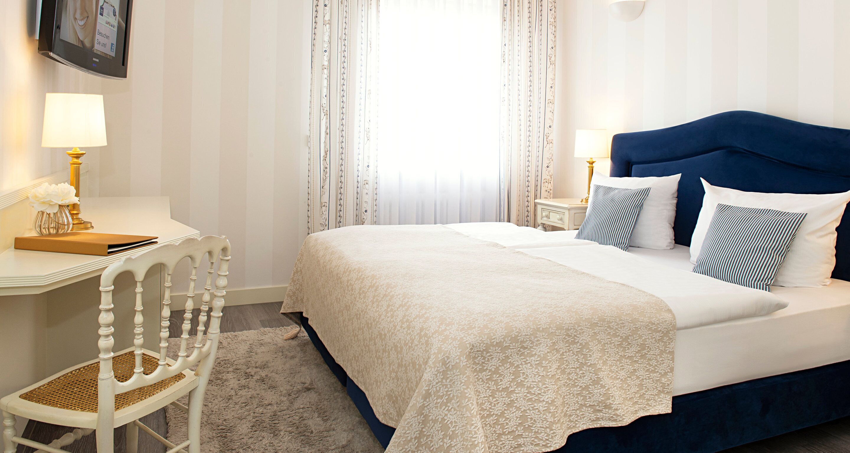 Ein ordentlich eingerichtetes Hotelzimmer mit Bett, Nachttischen, Schreibtisch und Stuhl.