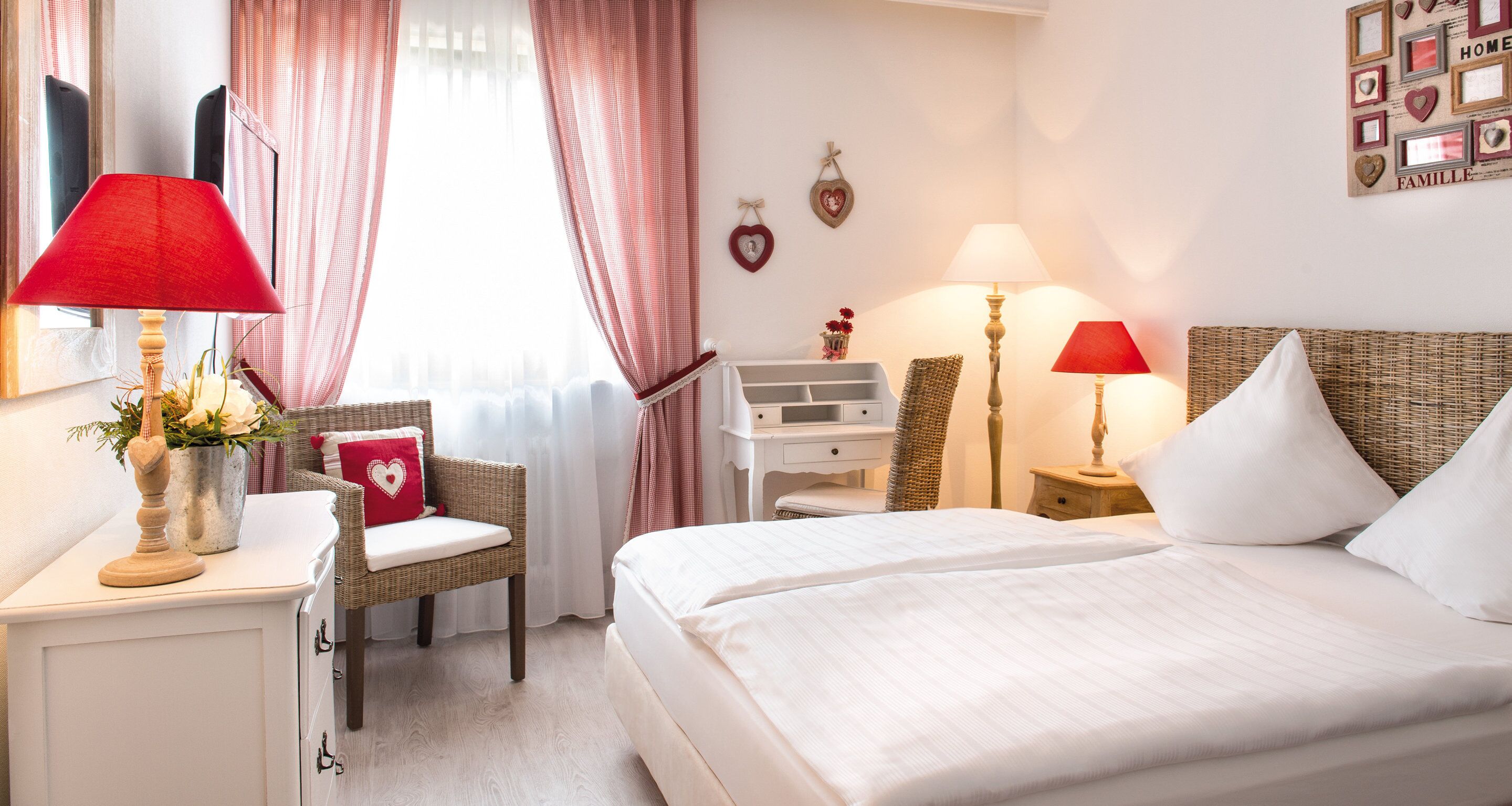 A hotel room with a bed, two bedside tables with lamps, a chair, a small white dresser, and a window with curtains.