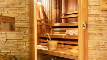 Eine Holzsauna mit Bänken und einem Eimer vor einer Steinwand.