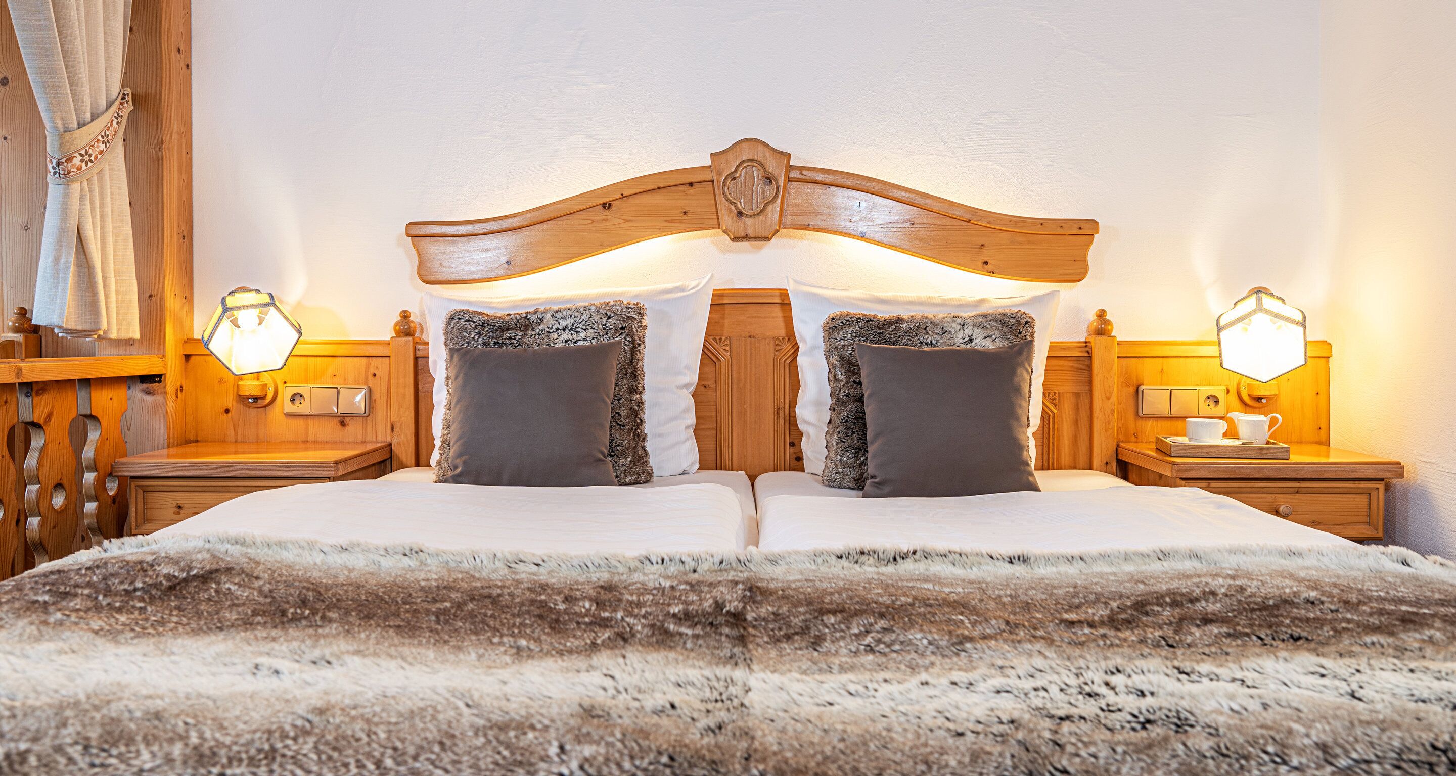 Una cama doble con cabecera de madera, dos lámparas de noche y una manta de piel.