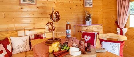 L’intérieur d’un chalet en bois, avec une table à manger dressée, où l’on voit des bretzels, du fromage et des saucisses.