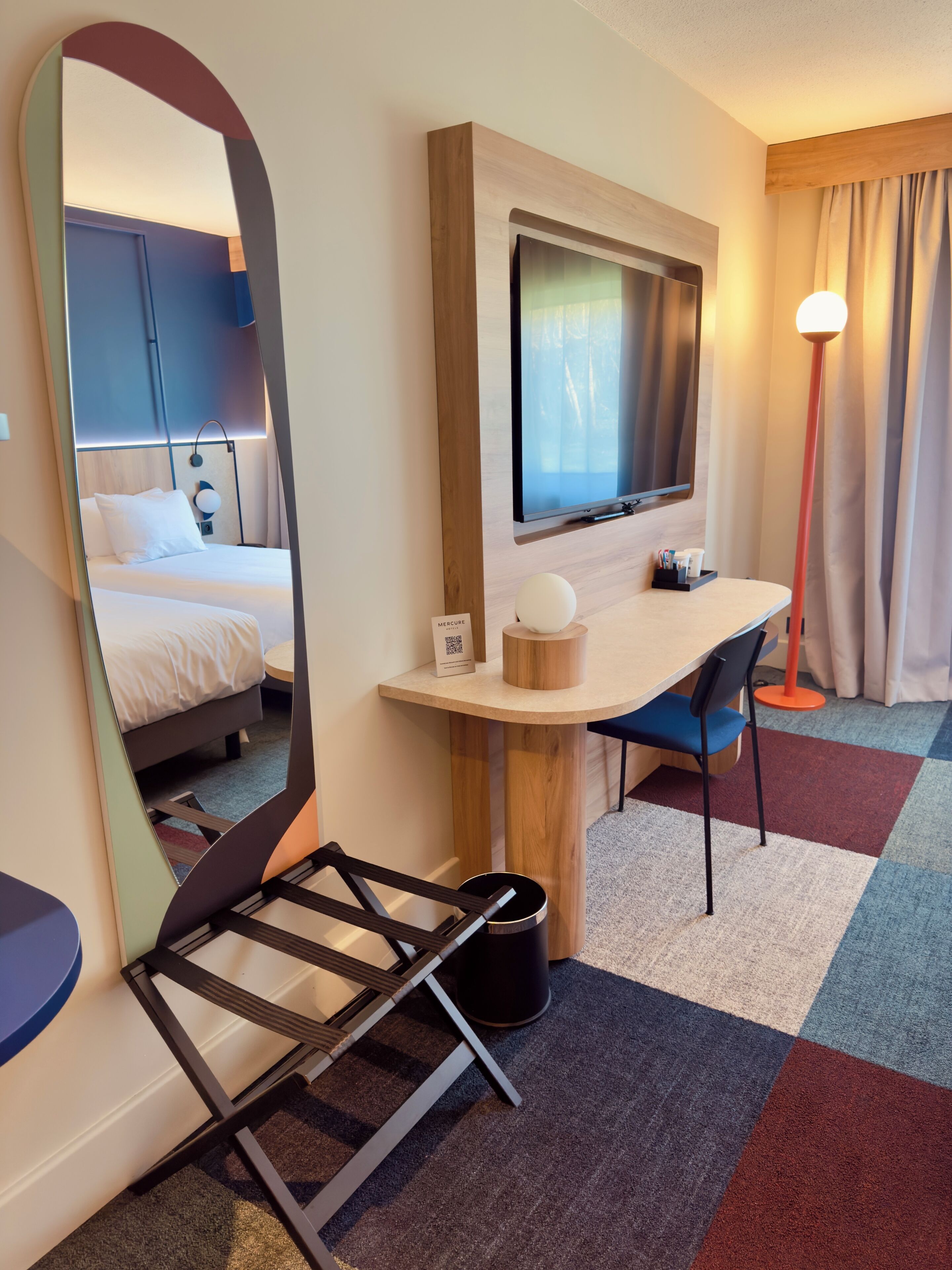 A hotel room with a bed, a desk with a chair, a TV, and a mirror.
