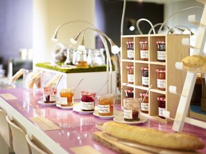 A food display with jars of preserves and a loaf of bread on a pink table. - Mercure Rouen Val De Reuil (Val-de-Reuil)