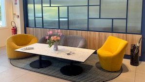 A modern room with a table, two yellow chairs, a vase with flowers, and a large window with a view. - Mercure Rouen Val De Reuil (Val-de-Reuil)