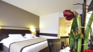 A hotel room with a bed, a chair, and a table with flowers. - Mercure Rouen Val De Reuil (Val-de-Reuil)