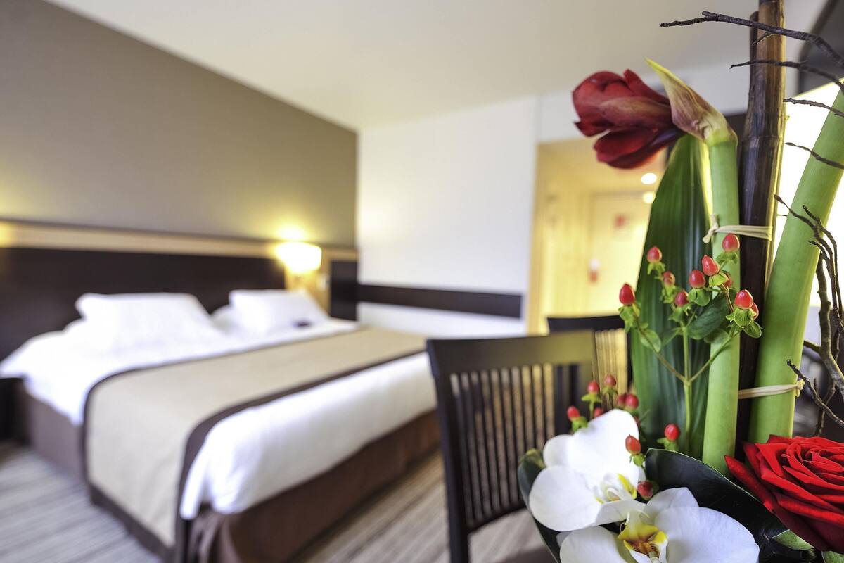 A hotel room with a bed, a chair, and a table with flowers.