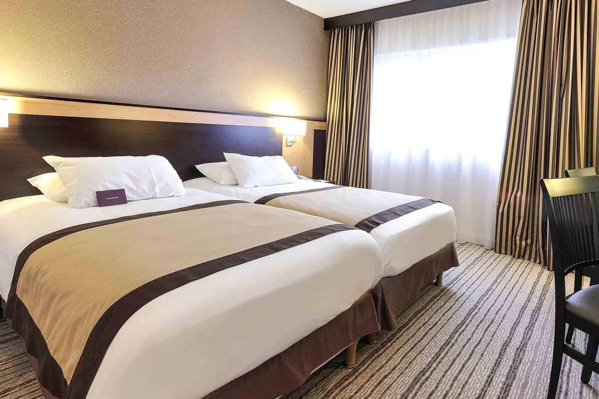 A hotel room with two beds, a headboard, a window with curtains, and a carpeted floor.