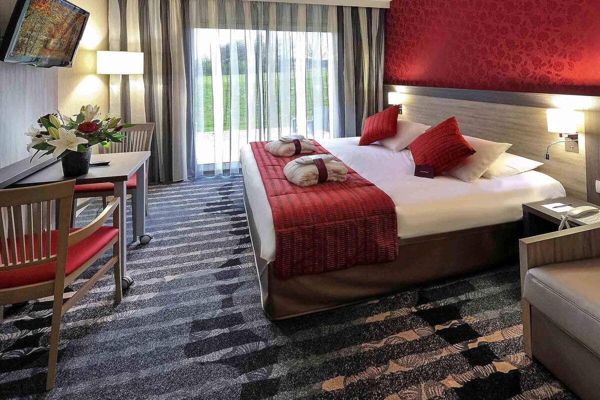 A hotel room with a bed, a desk, a chair, a TV, and a window with curtains.
