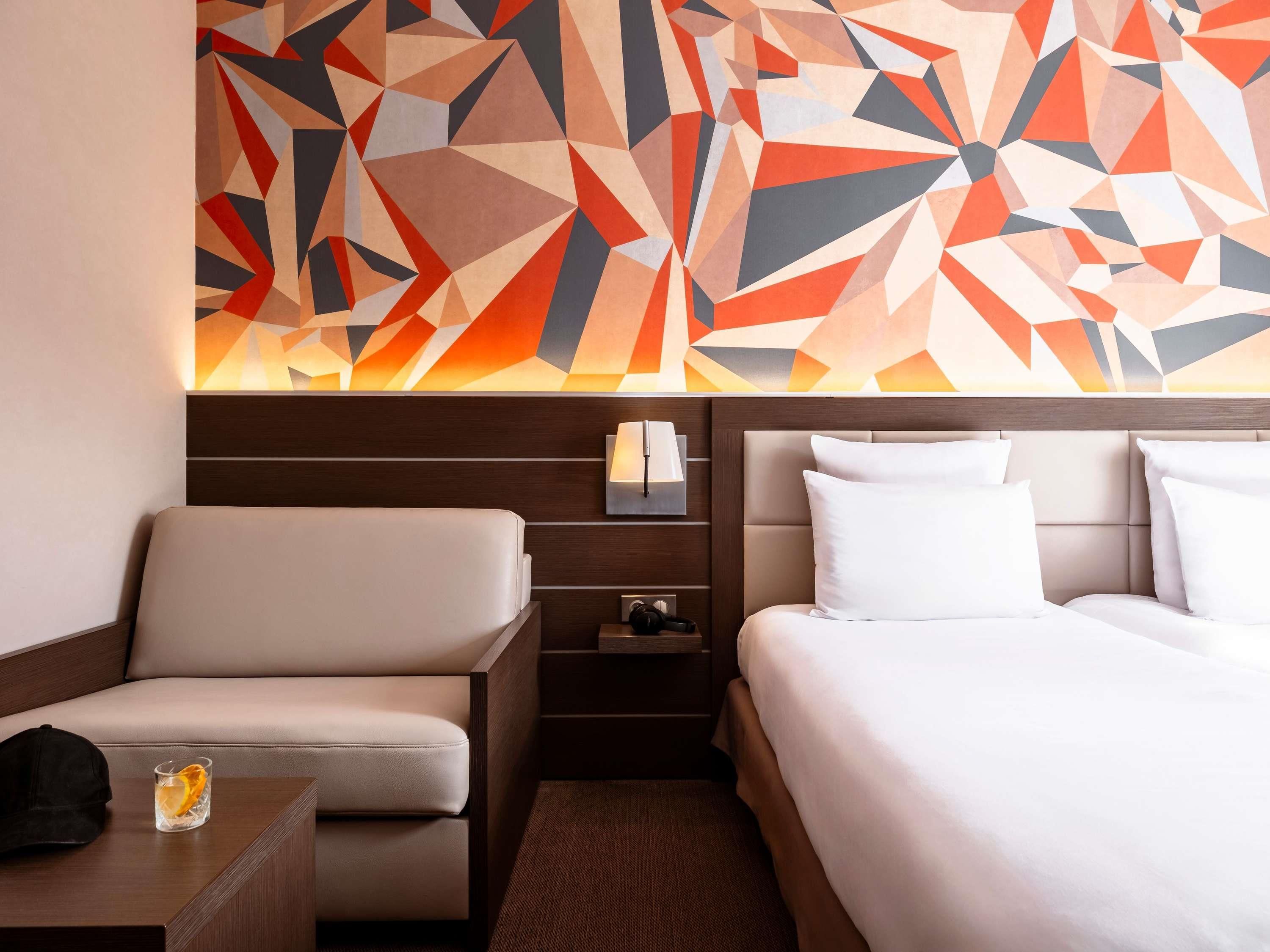 Ein Hotelzimmer mit Bett, Sofa, Nachttisch und einer Wand mit geometrischer Kunst.