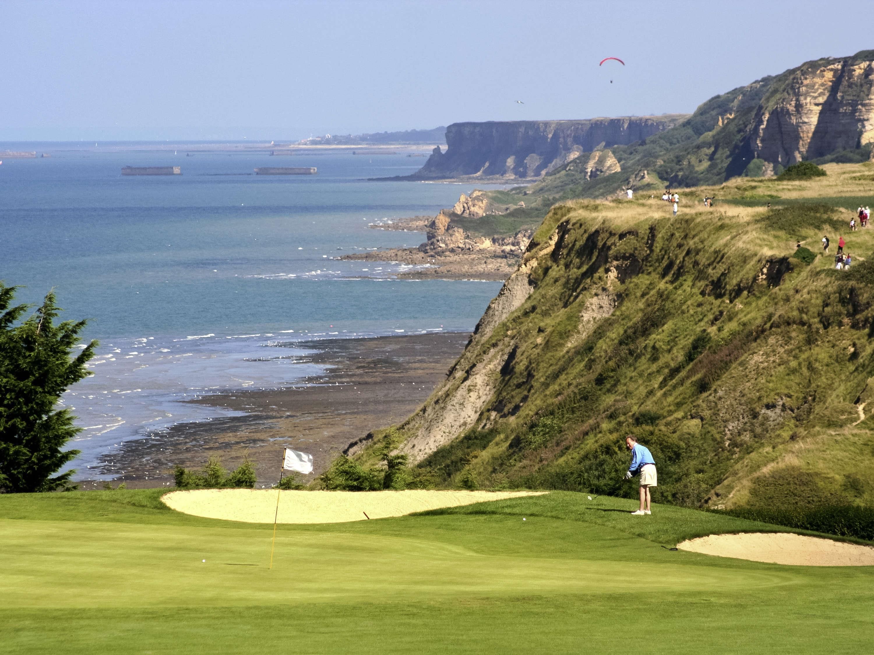 A golf course with a flagstick, sand bunkers, and a view of the ocean and cliffs.