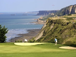 A golf course with a flagstick, sand bunkers, and a view of the ocean and cliffs.