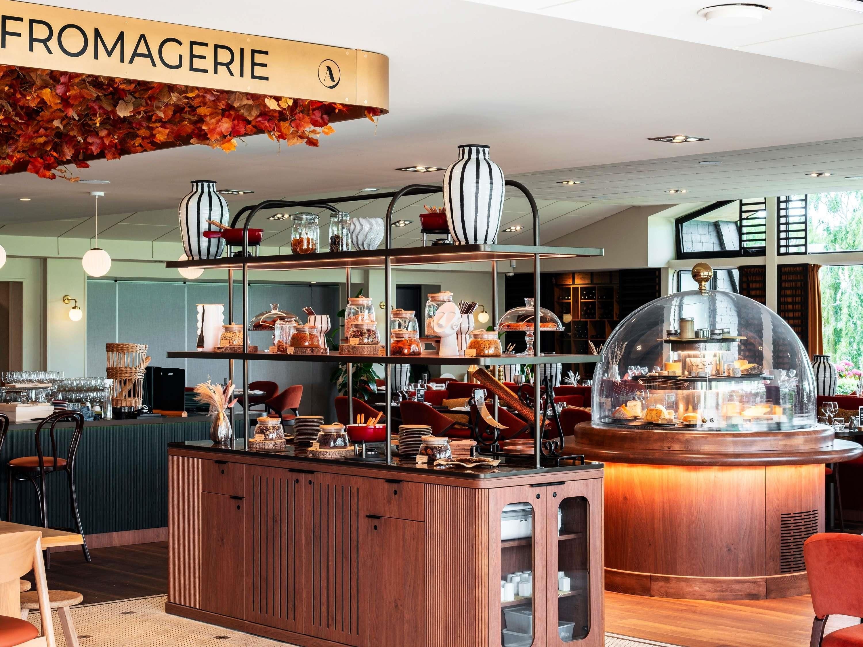 A cafe with a sign reading 'FROMAGERIE,' shelves with jars and glasses, and a display case with pastries.