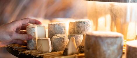 A hand holding a cheese wheel, surrounded by other cheese wheels on a wooden board.