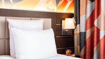 Una habitación de hotel con cama, almohadas, mesita de noche, lámpara y cortinas.