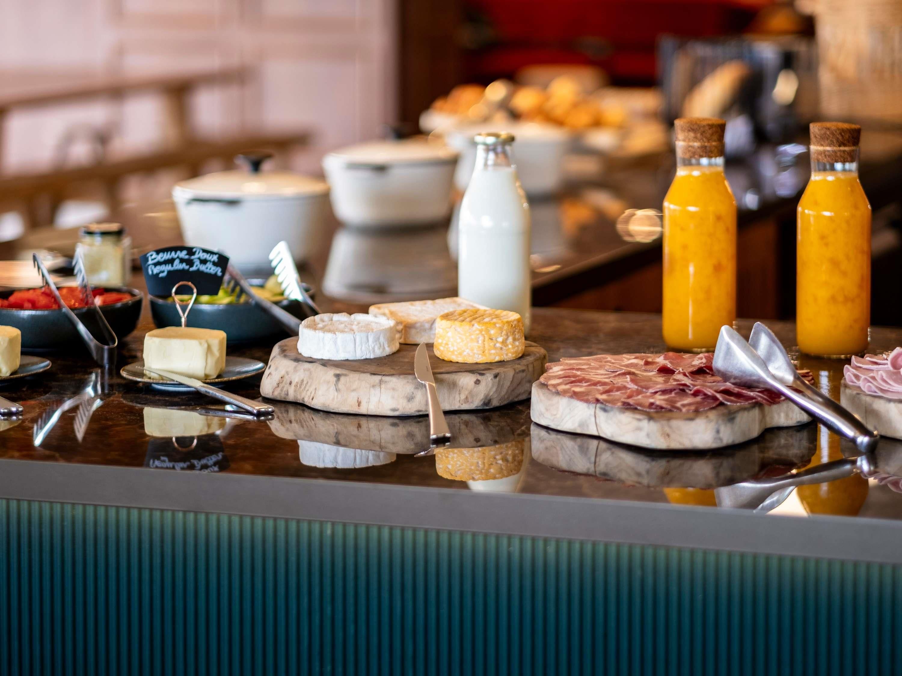 A buffet with various cheeses, meats, and a milk jug.