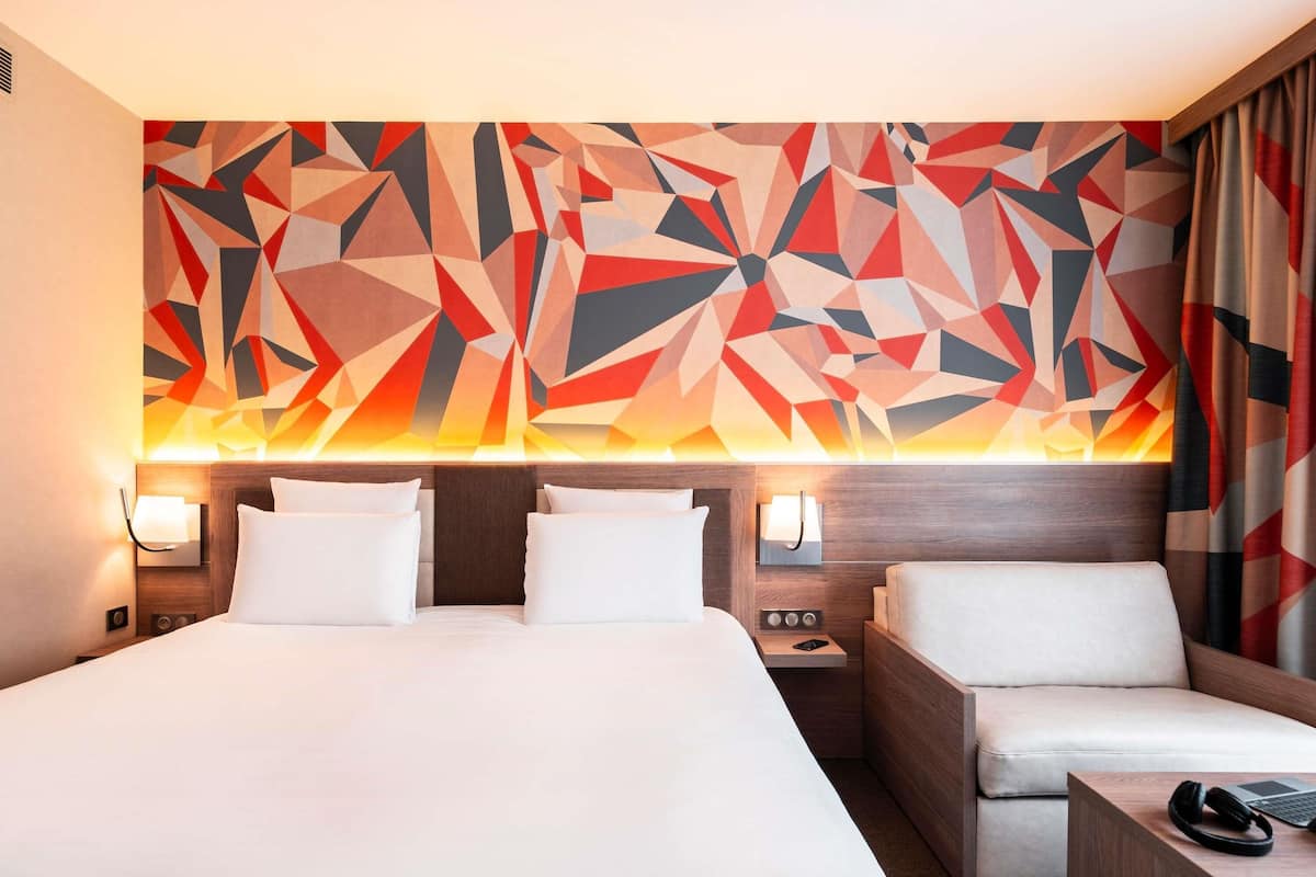 A hotel room with a large bed, two bedside tables, a sofa, and a geometric wall mural.