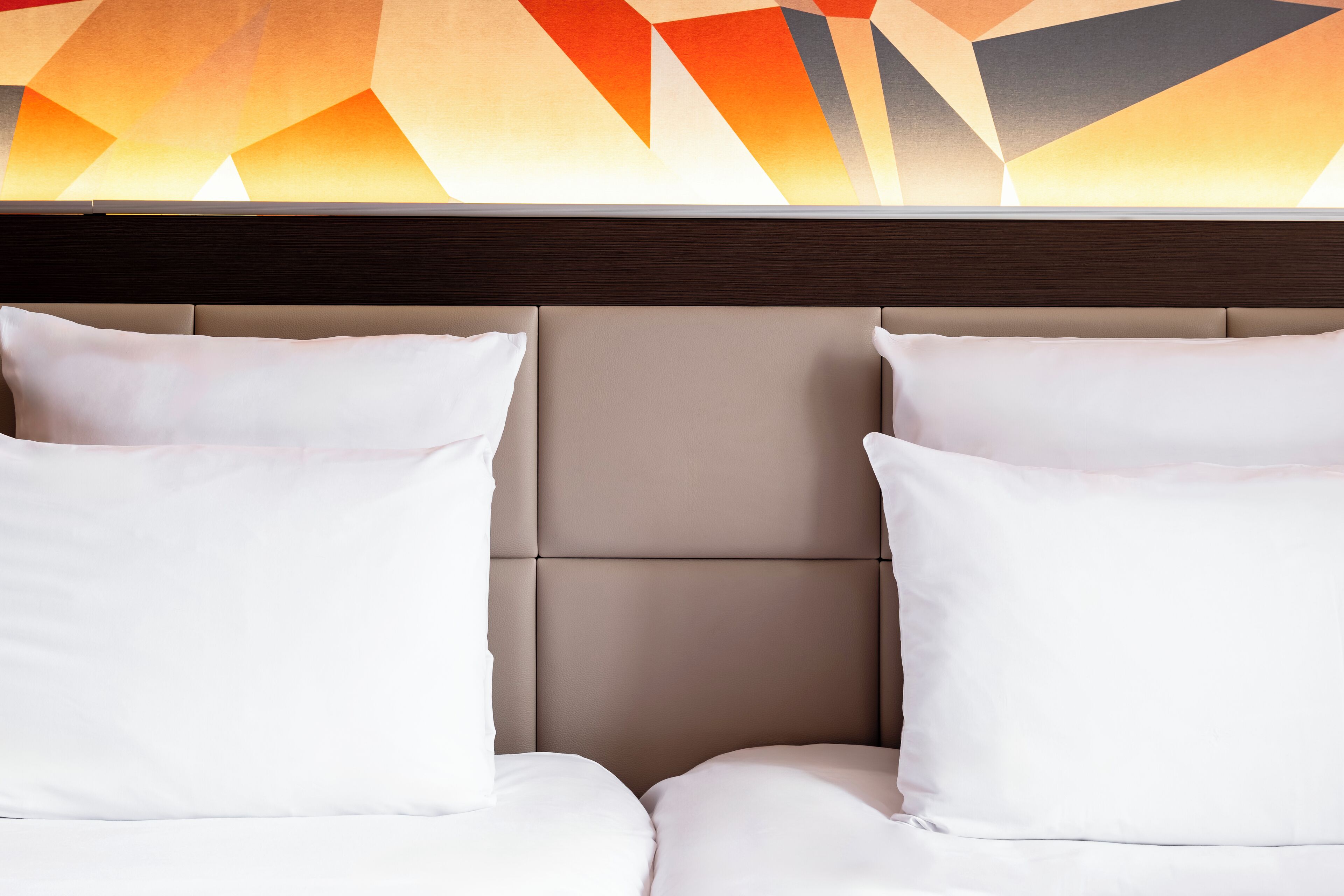 Habitación de hotel con cabecera y dos almohadas blancas.