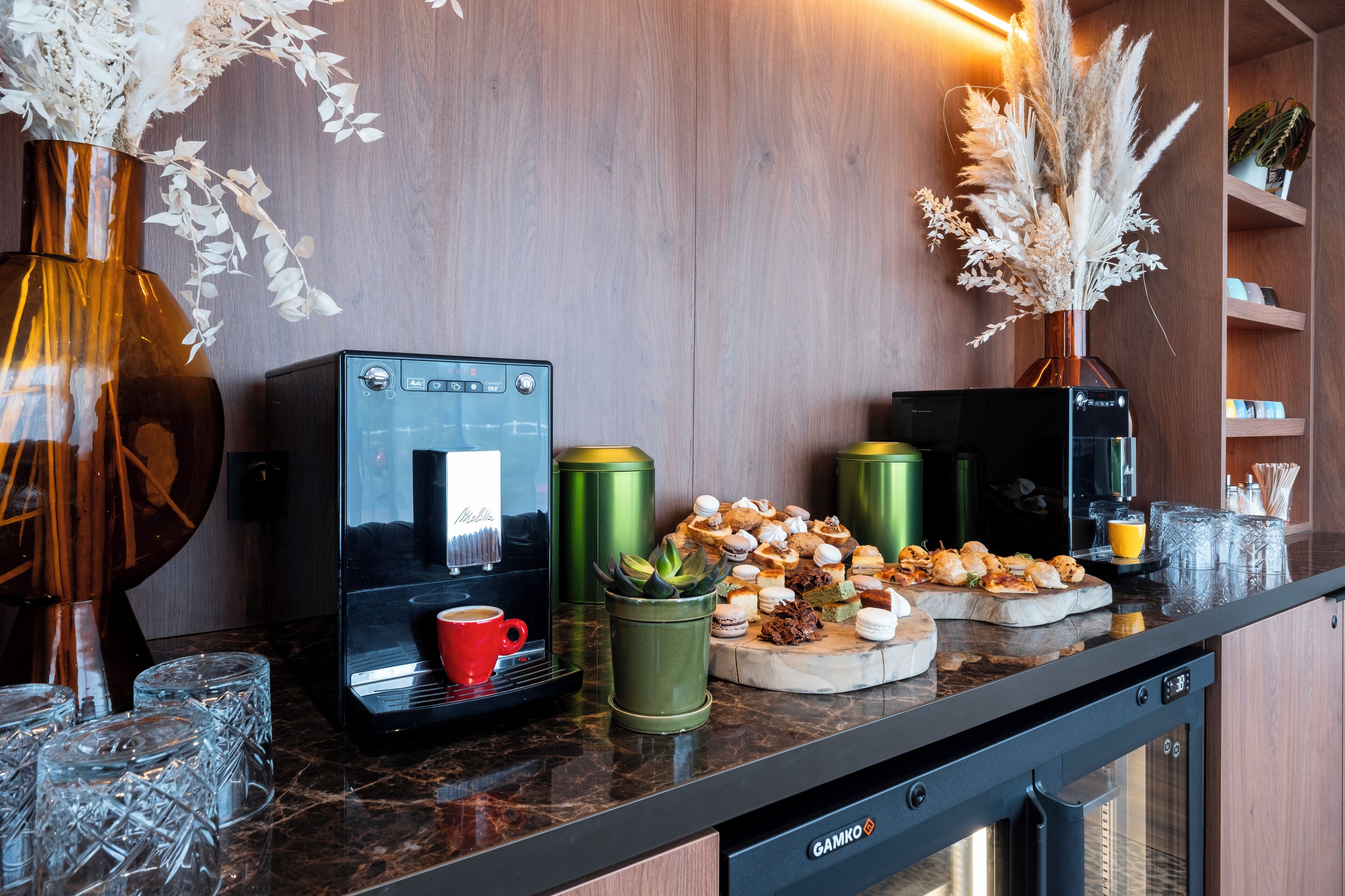 A kitchen counter with a coffee machine, a red mug, and a variety of pastries.