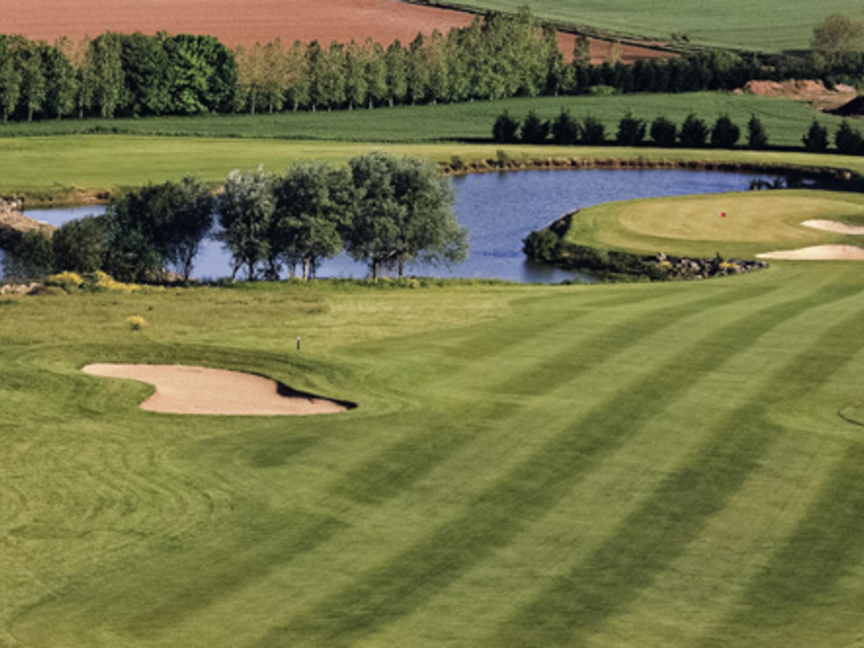 En golfbane med sandbunker, et bassin og træer.