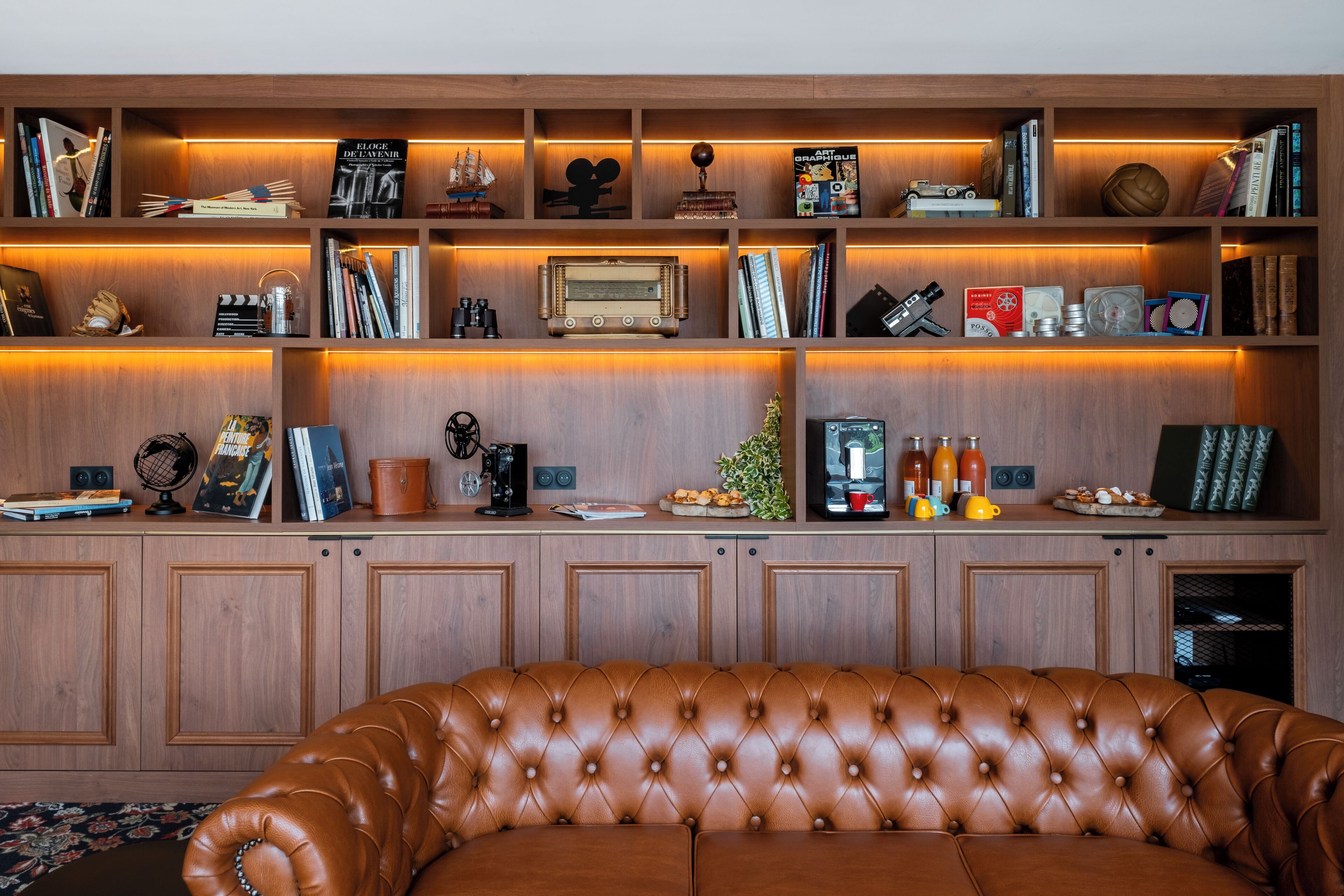 Une pièce avec un canapé en cuir marron, des étagères en bois ornées de livres et d’objets décoratifs, et un meuble en bois.